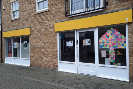 Image showing number 7 Crown Street, Brentwood - a brick building with yellow signage.  In one of the windows, colourful notes are displayed.