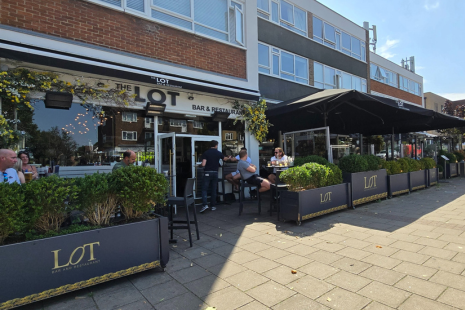 Exterior image of The Lot Bar & Restaurant in Shenfield, showing outdoor planters and large black parasols over dining areas.