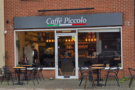 Exterior of Caffé Piccolo with brick wall, outdoor seating, and large windows.