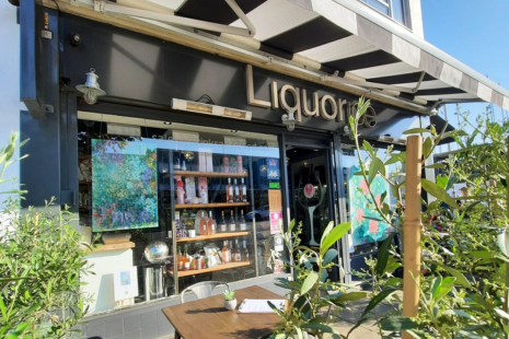 Image of the exterior of Liquorice Wine & Deli in Ingatestone.  Black and white awning can be seen, along with artwork in the window, tables and chairs outside and shelves of products in the window