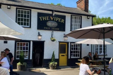 Image of the exterior of The Viper pub , a white traditional building with a yellow door.  People are sitting underneath parasols outside.