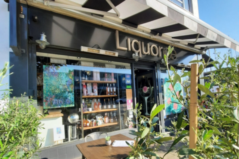 Image of the exterior of Liquorice Wine & Deli in Ingatestone.  Black and white awning can be seen, along with artwork in the window, tables and chairs outside and shelves of products in the window
