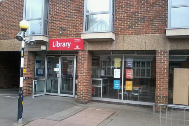 Image of the exterior of Ingatestone Library, a brick build building, with a red sign.  A lamp-post for a zebra crossing is visible in the image.