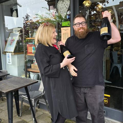 Jo and Dan at Liquorice Wine & Deli celebrating by holding a large bottle of champagne.