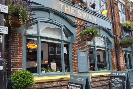 Exterior of The Swan pub in Brentwood High Street, the windows and long sign are painted green.  THE SWAN is in gold lettering.